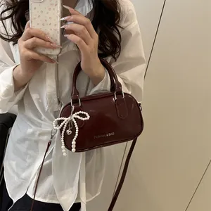 Sac à main rouge foncé en cuir verni avec perle nœud porté par un mannequin