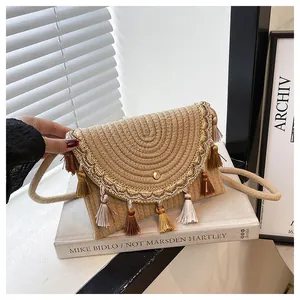 Detail of straw woven envelope bag with boho tassels and golden embroidery accents