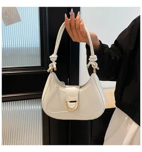 Close-up of a white hobo bag with gold hardware and knot handle detail in hand