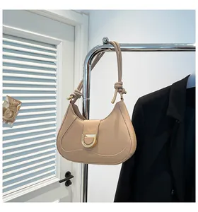 Detail of beige crescent underarm bag featuring a gold D-ring buckle and knotted strap