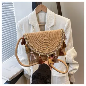 Detailed close-up of straw woven crossbody bag with brown tassels and lace embroidery edge