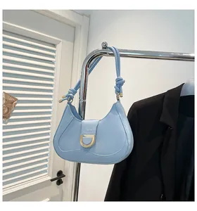 Close-up of baby blue crescent shoulder bag featuring a gold D-buckle and knot detail