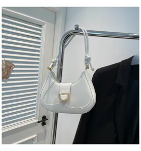 Detail of white half-moon saddle bag with gold U-shaped buckle and knotted shoulder strap