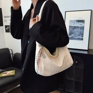 Detail of off-white hobo bag with wide shoulder strap and woven pendant charm