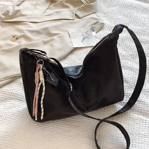 Macro view of black suede half-moon bag featuring decorative woven tassel charms