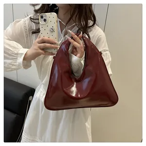 Detail einer tiefroten Handtasche aus Glanzleder mit elegantem Griff und moderner Form