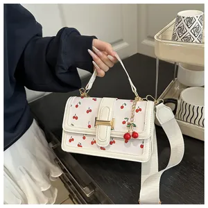 Detail of white leather handbag featuring red cherry prints and golden metal clasp lock