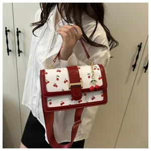 Detailed close-up of white crossbody bag with red cherry prints and gold metal buckle