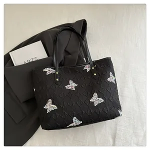 Close-up of quilted black tote bag featuring colorful butterfly embroidery and leather strap