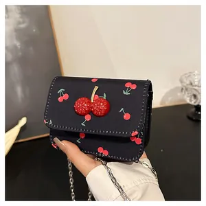 Detail of black cherry print crossbody bag featuring a 3D red cherry charm and chain