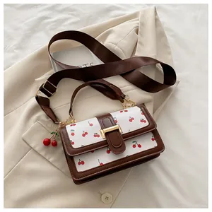 Close-up of white small crossbody bag with red cherry pattern and brown leather straps
