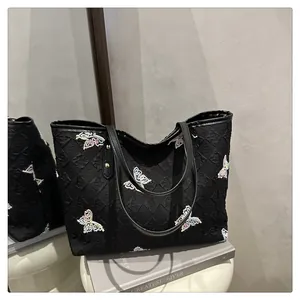 Detail view of black tote bag with sequin butterfly and textured monogram pattern