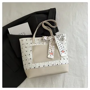 Detail of cream tote bag with embossed texture, smooth pockets, and floral scarf accessory