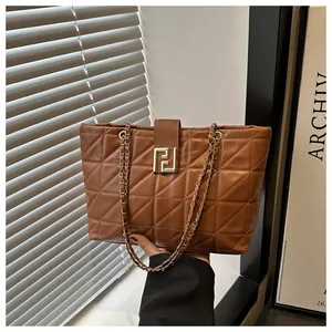 Detail of brown quilted tote bag showing golden geometric turn-lock and chain strap