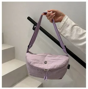 Detail of light purple crescent shoulder bag with metallic logo on a modern gray backdrop