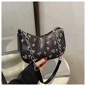 Detail view of black faux leather shoulder bag with red cherry prints and silver chain strap