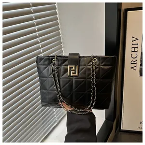 Detail of black quilted shoulder bag featuring gold geometric clasp and chain strap