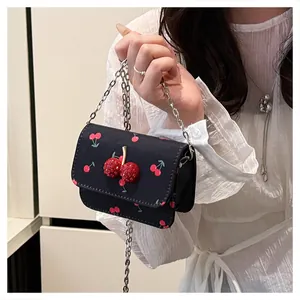 Detail of a black crossbody bag with red cherry patterns and a 3D cherry buckle