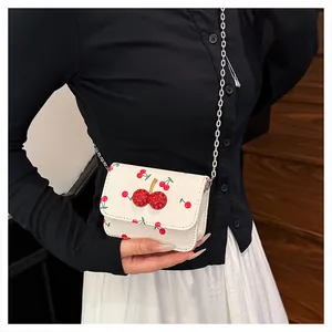 Detail of a white crossbody bag with cherry prints and a red rhinestone cherry clasp