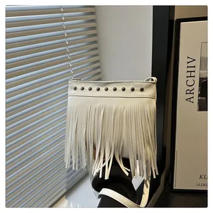 Detalle de bolso de hombro blanco con flecos, tachuelas negras y textura de cuero granulado