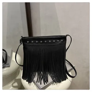 Detalle de bolso en cuero negro con tachuelas metálicas y flecos largos estilo boho