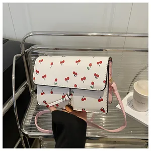 Détail d'un sac bandoulière blanc avec motifs cerises et pendentif en métal doré