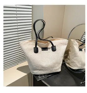 Detail of a large woven tote bag with black handles and a minimalist leather patch