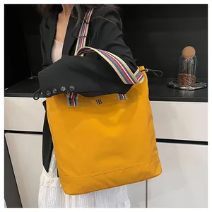 Detail of yellow canvas tote bag with colorful striped strap and metal logo accent