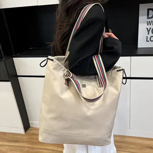 Minimalist beige canvas tote bag with striped shoulder strap and drawstring detail