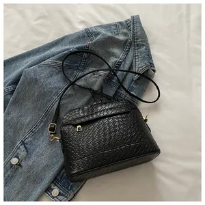Detail of black woven texture shell bag with gold hardware on denim background