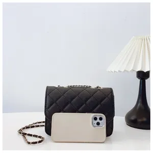 Quilted black chain bag size comparison with a smartphone on a minimalist background