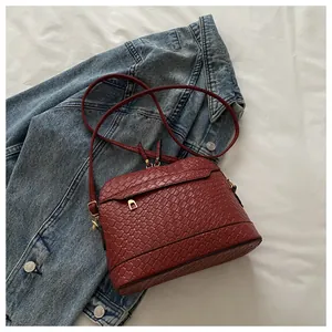 Detail of burgundy shell bag with woven texture on denim background showing gold zippers