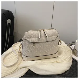 Detail of white crocodile embossed shell bag with gold hardware on satin fabric