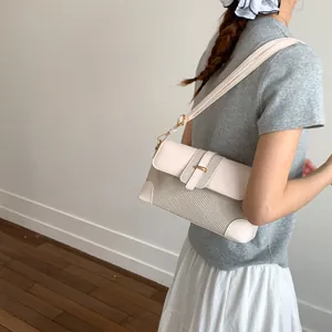 Vue latérale du mannequin portant un sac bandoulière beige tissé avec boucle dorée
