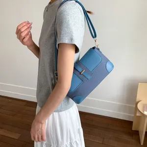 Détail d'un sac à bandoulière en cuir bleu avec boucles dorées porté par un mannequin