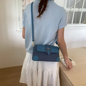 Détail d'un sac à main bleu en patchwork avec boucle dorée sur une table sobre