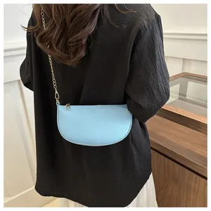 Detail der hellblauen sichelförmigen Ledertasche mit goldener Kette an der Modelschulter
