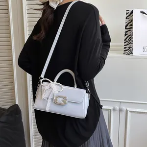 Detail view of light grey patent leather handbag with pearl charm and metal buckle