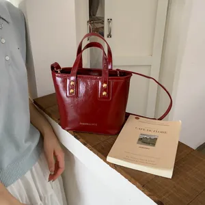 Detail of red glossy bucket bag with golden rivets and adjustable strap on a wood step