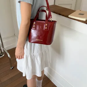 Detail of burgundy bucket bag with glossy texture and gold metal studs on a model