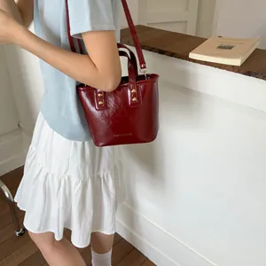 Detail of burgundy glossy bucket bag featuring gold studs and adjustable shoulder strap