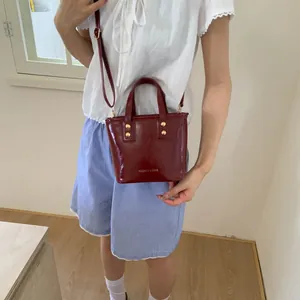 Burgundy polished leather bucket bag shown with golden studs and fashion logo on model