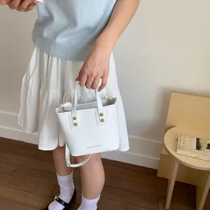 Close-up of white leather bucket bag with gold accents and detachable shoulder strap