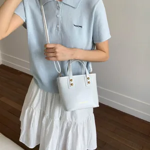 Detail of white bucket bag with gold studs and short handle shown from a top-down view