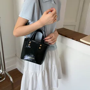 Detail of glossy black mini bucket bag featuring gold rivets and logo on minimalist model