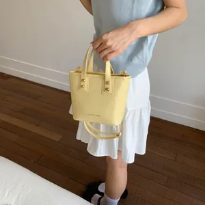 Light yellow bucket bag with golden rivets and top handles shown on model in studio