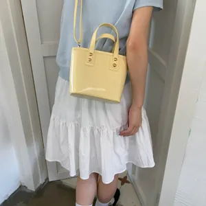Detail of pale yellow patent leather mini bucket bag with gold rivets on summer outfit