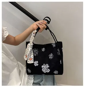 Détail d'un sac cabas floral noir avec anses tressées et accessoire foulard en soie