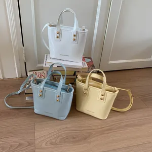 Three fashion bucket bags in white, blue, and yellow with gold rivets on display