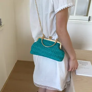 Detail of turquoise woven crossbody bag with gold metal frame and chain on white dress